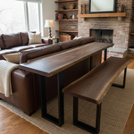 Solid wood live edge bar table in walnut color finish with black steel legs and matching bench, styled behind leather sofa near fireplace