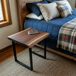 Solid wood live edge side table in walnut color finish beside bed with blue bedding, black metal legs