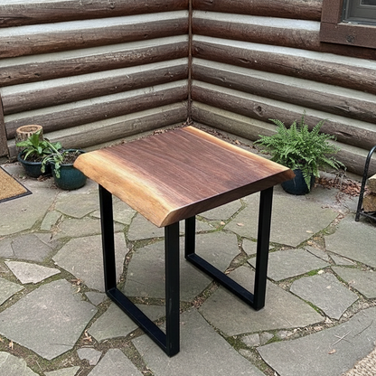 Solid wood live edge side table in walnut color with black steel legs placed on outdoor stone floor near log wall